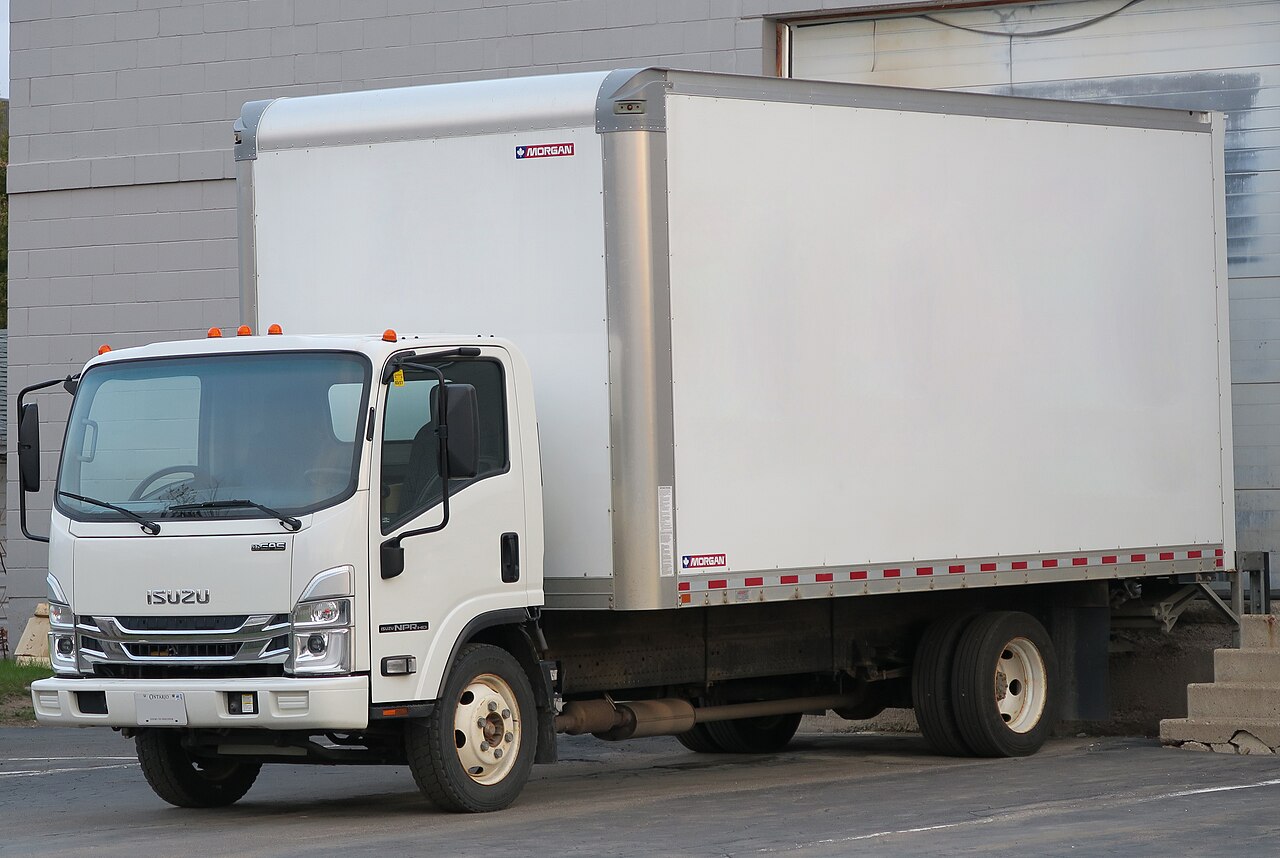 White Isuzu NPR-HD box truck parked beside a building