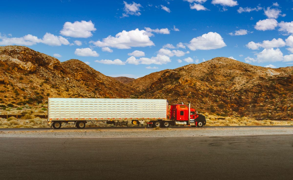 Red semi-truck pulling an enclosed trailer on a highway